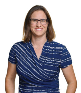 headshot for a smiling woman in glasses and a blue striped top
