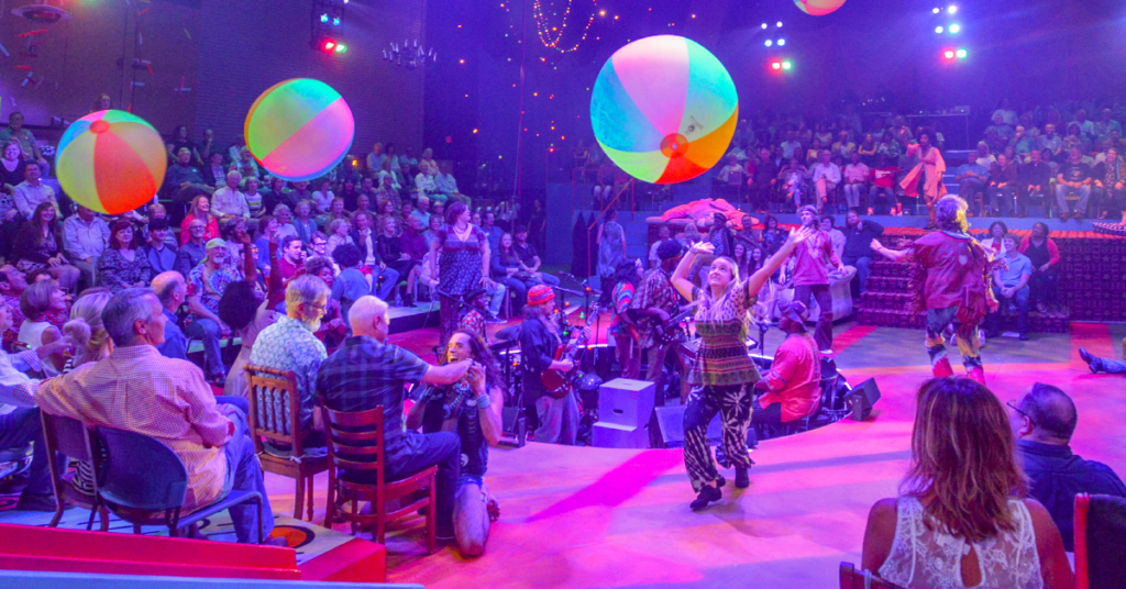 audience watching a play with musicians and actors passing around beach balls