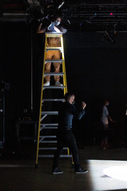 student on top of a ladder focusing a lighting instrument