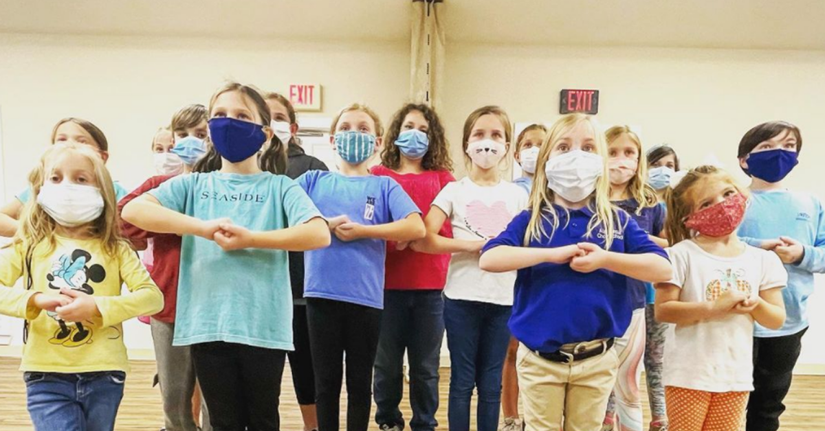 a group of children standing and singing while wearing masks