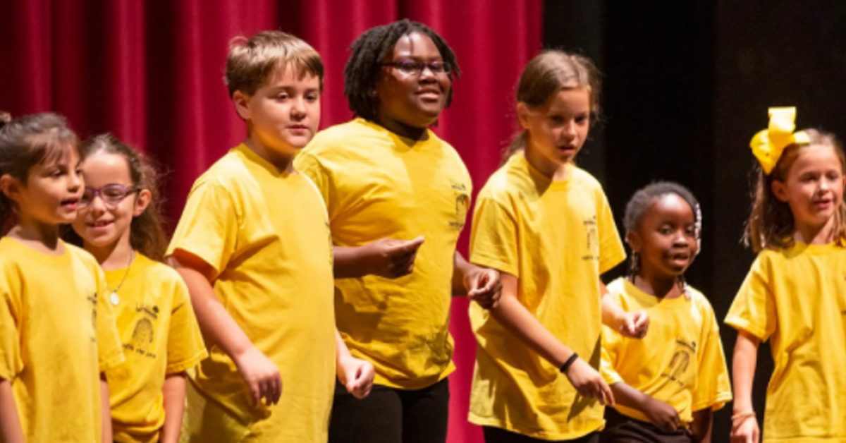 a group of children on stage dancing in yellow t-shirts