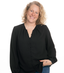 Erin Breitenbach headshot: a standing woman with dark top, curly hair, and a hand in her pocket