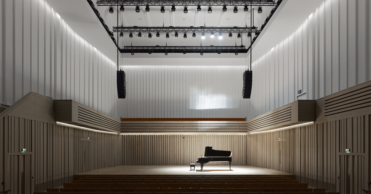 grand piano on a stage sitting beneath speakers and lights