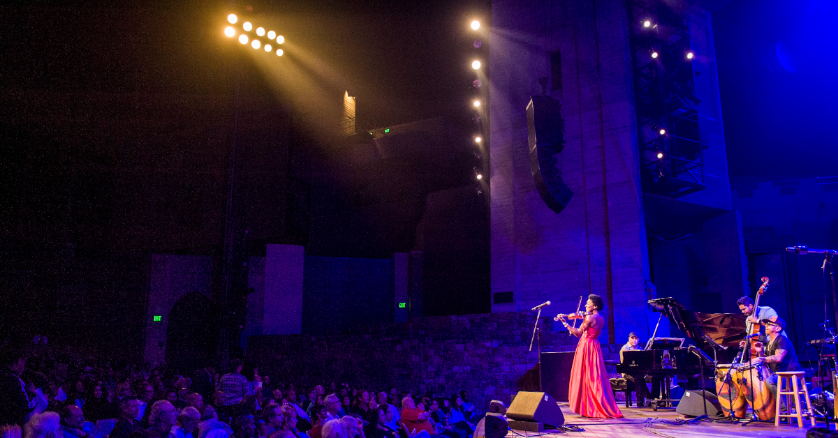 fiddle player on stage in a red dress while stage lights shine down