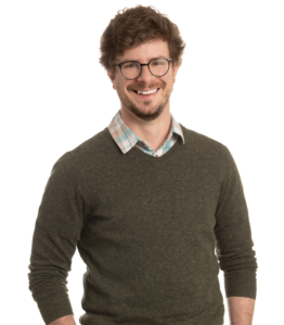 man in glasses and a green sweater facing the camera and smiling