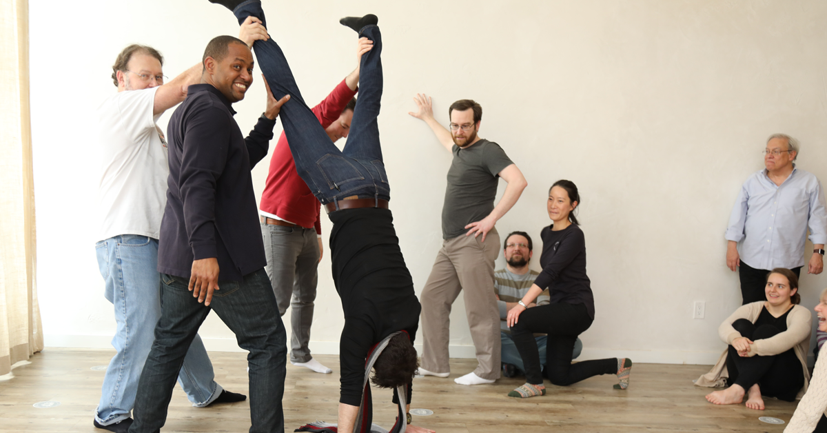 a group of people work on a dance exercise with one employee doing a hand stand