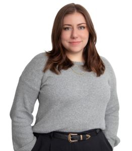 woman in grey sweater and black pants facing the camera in front of a white backdrop