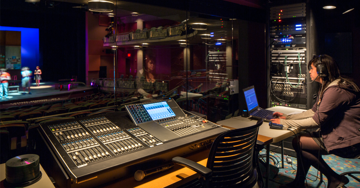 student seated in theatrical control booth in front of boards
