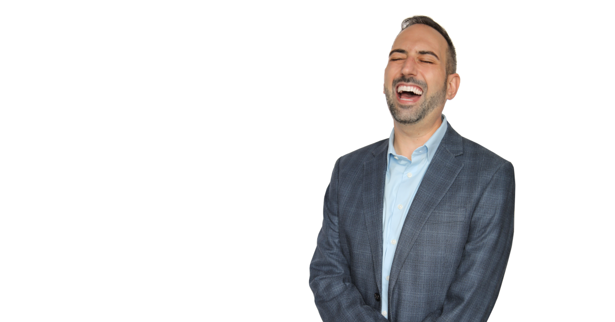 man in blue sports coat laughing against a white backdrop